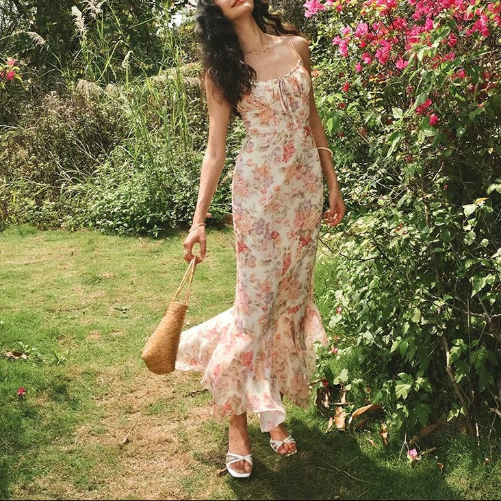 Woman in a floral dress standing in a garden with flowers and greenery.